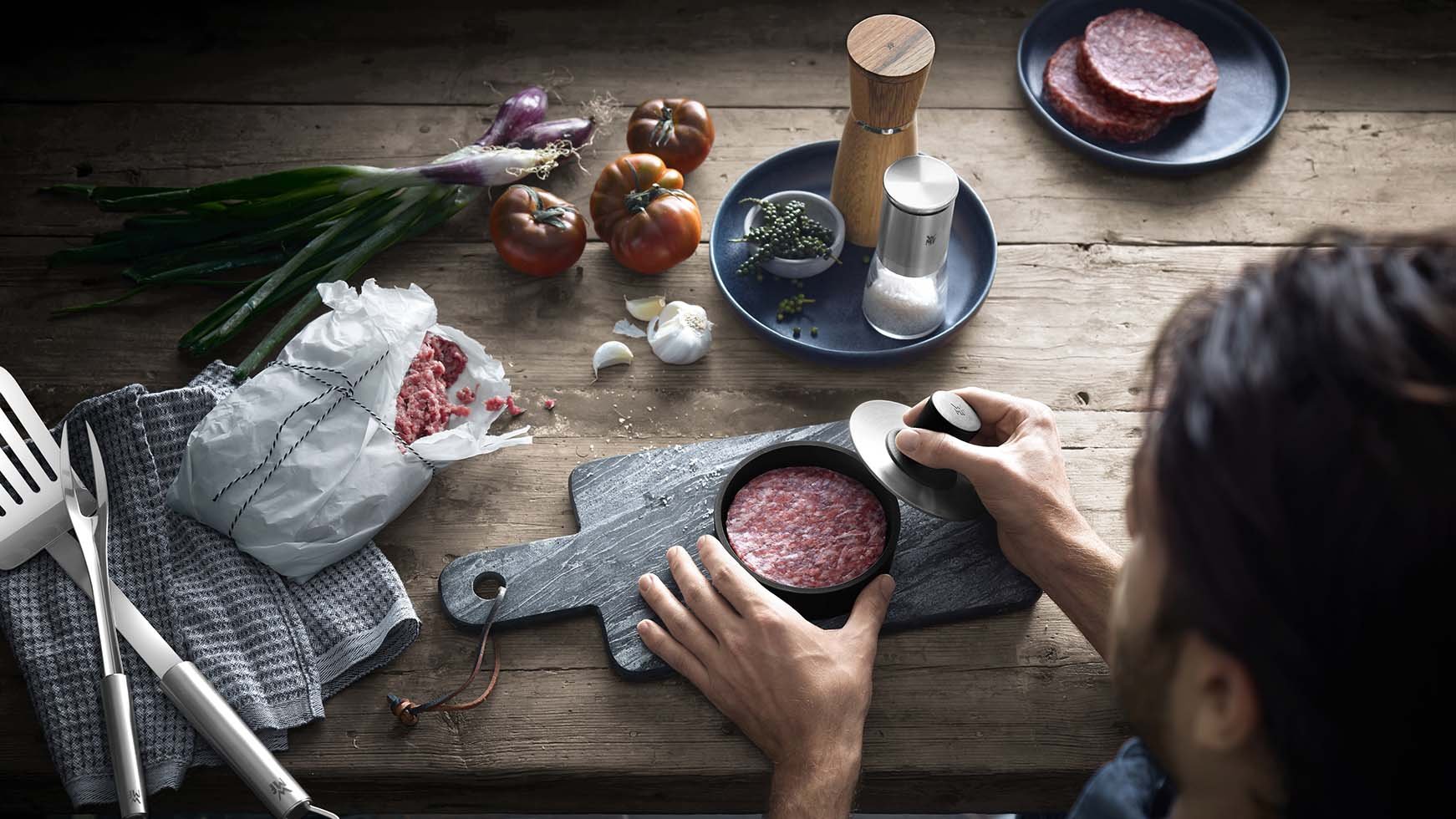 Einer Person bei der Zubereitung von Grillfleisch mit WMF Zubehör. Drumherum auf dem Tisch sind verschiedene Gewürze zu sehen. 