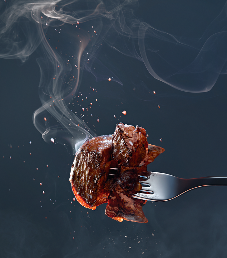 Auf einer Gabel aufgespießtes, gebratenes, dampfendes Fleisch auf dunkelblauem Hintergrund