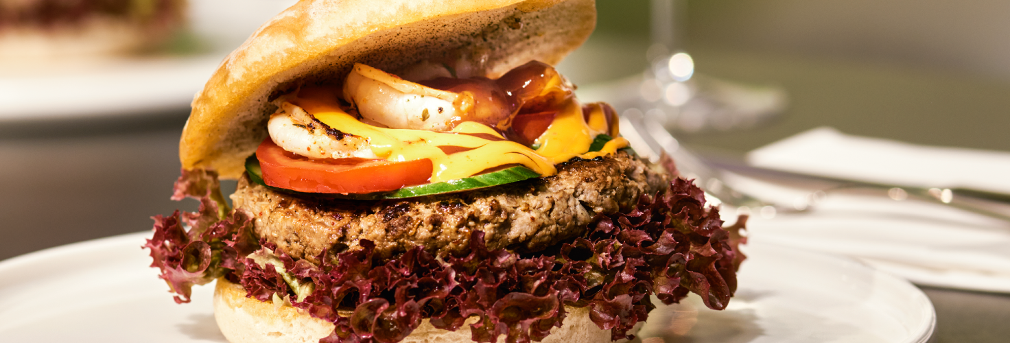 Burger auf einem weißen Teller und ein Weinglas