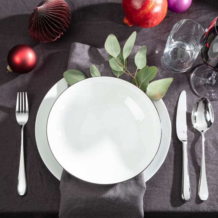 Weihnachtlich gedeckter Tisch mit grauer Leinentischdecke, Granatapfel, Weihnachtsschmuck und Eukalyptus-Zweig