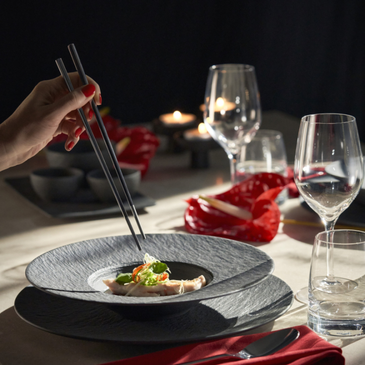 Schwarzer Teller mit asiatischem Essen, das mit Stäbchen gegessen wird